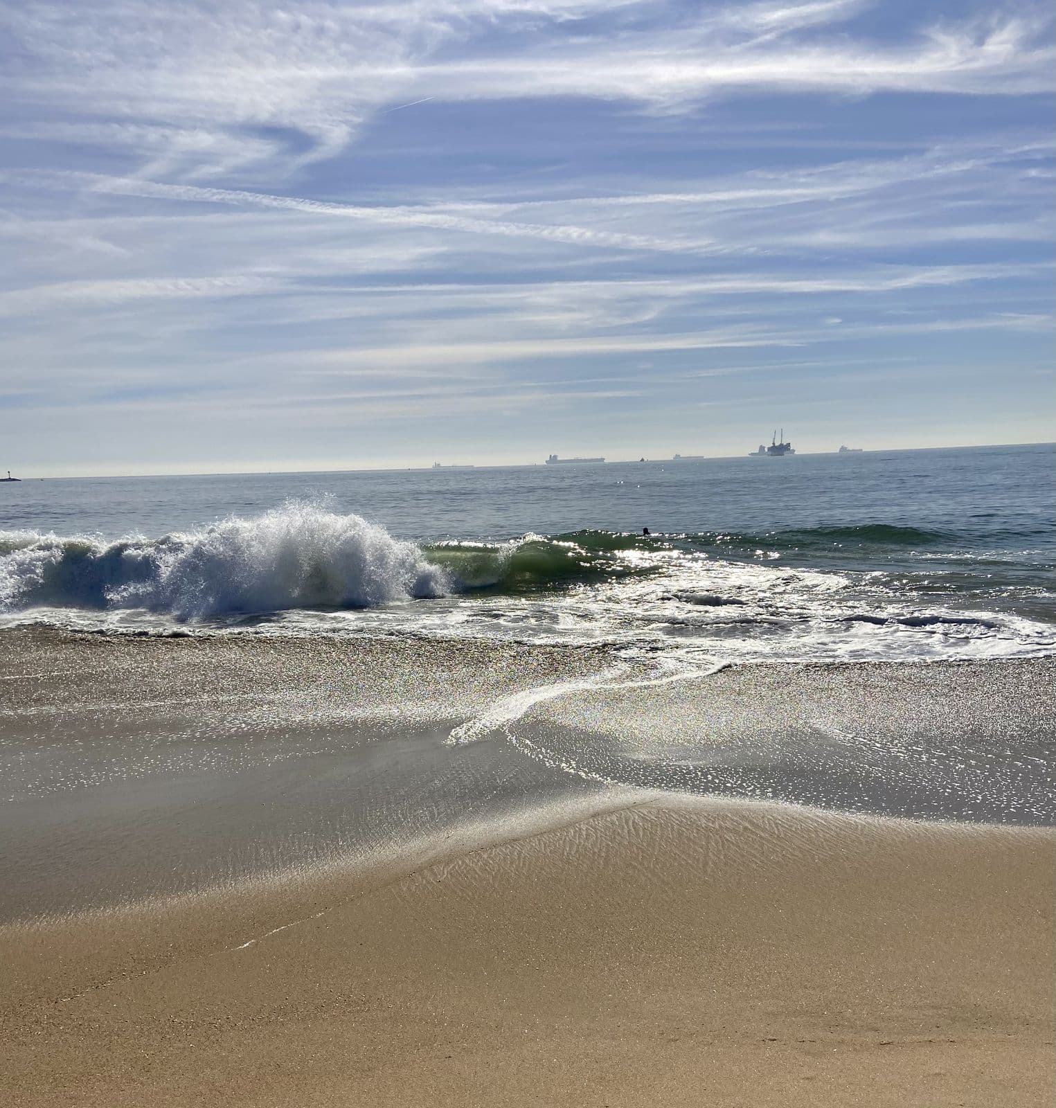 A wave folding onto the sand with ships on the horizon
