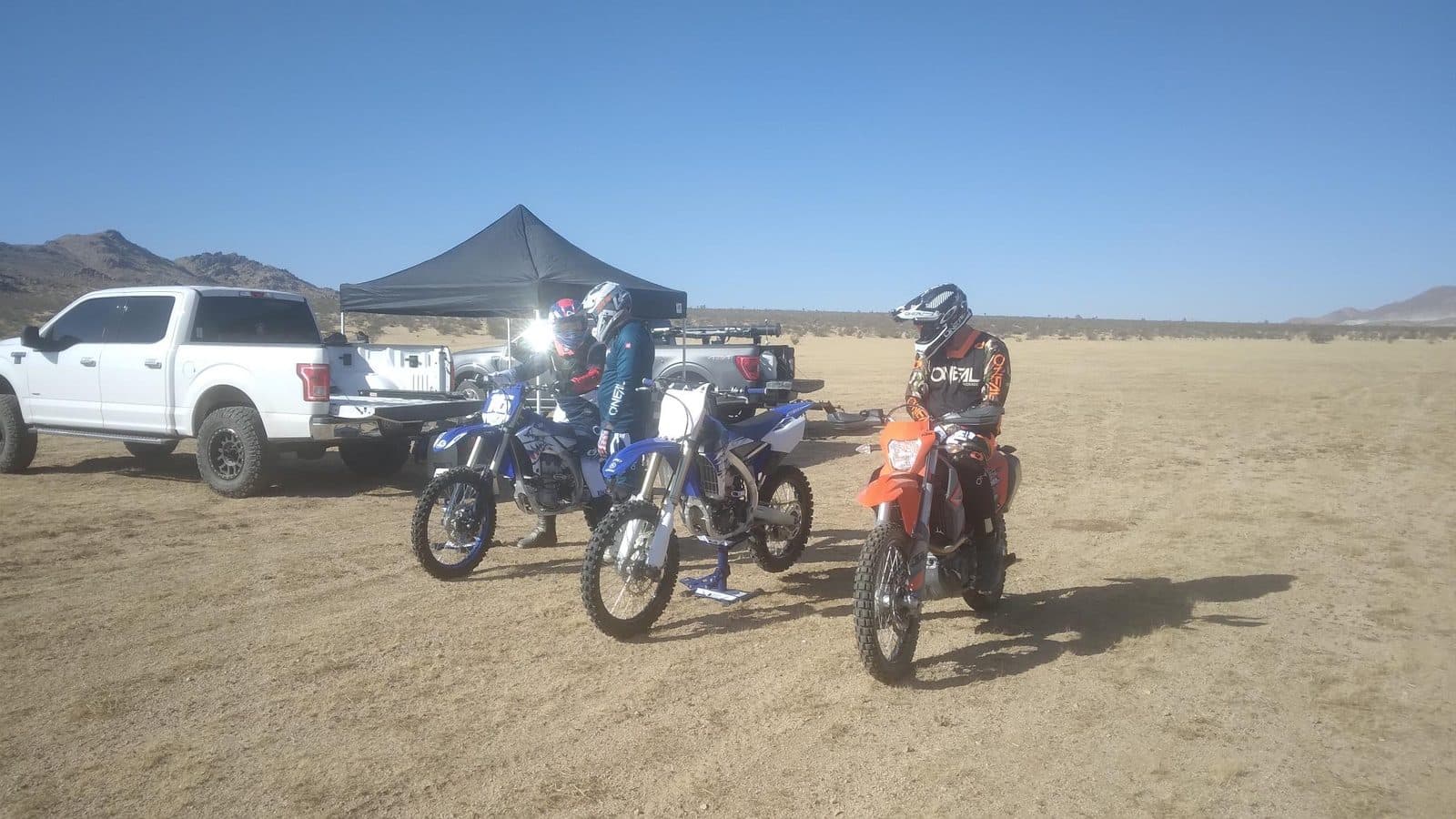 A truck, a shade canopy and two riders staged on a desert flat before a ride