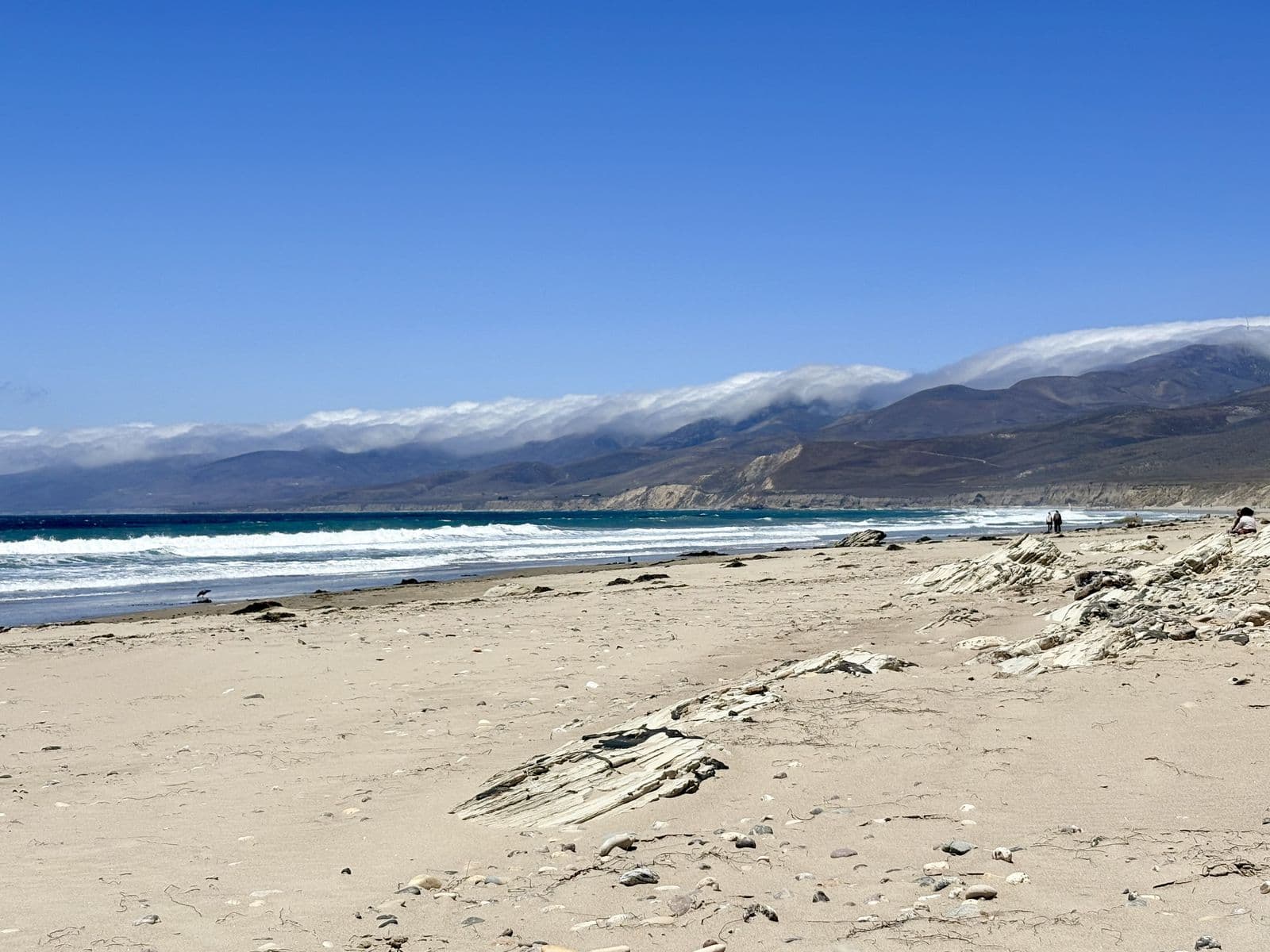 An empty beach with snow on the mountains behind it