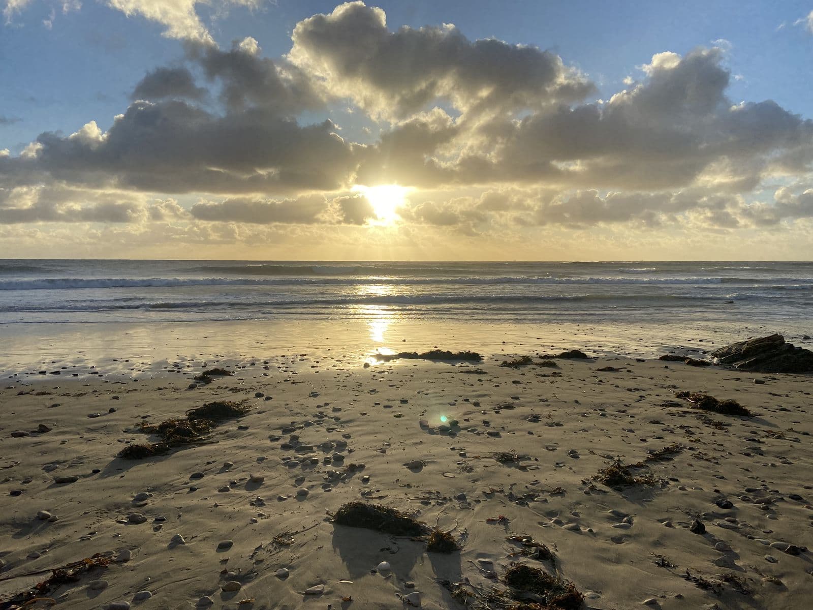 The sun breaking through clouds over wet sand at the end of the day