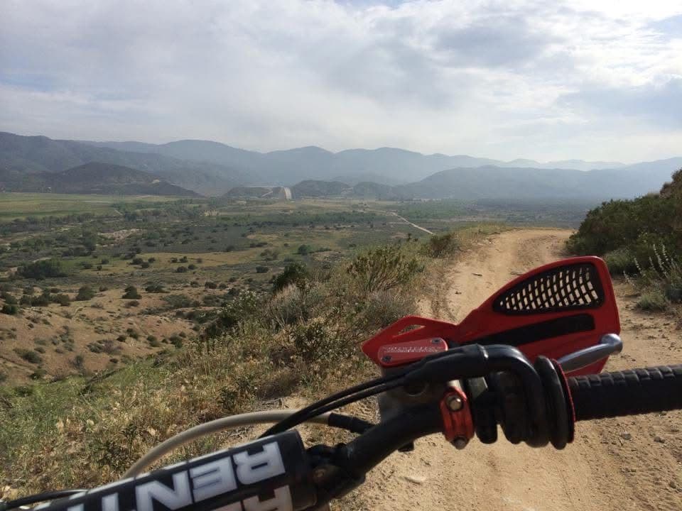 Dirt bike handlebars pointed down a trail toward a wide desert valley