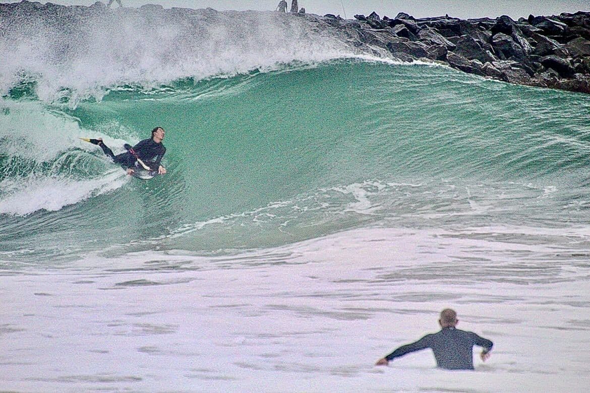 A bodysurfer tucked into a green barrel while someone watches from the whitewater