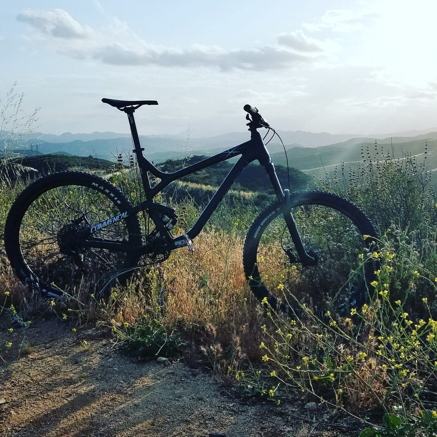 A mountain bike parked on a ridge trail at golden hour, ridgelines fading into haze